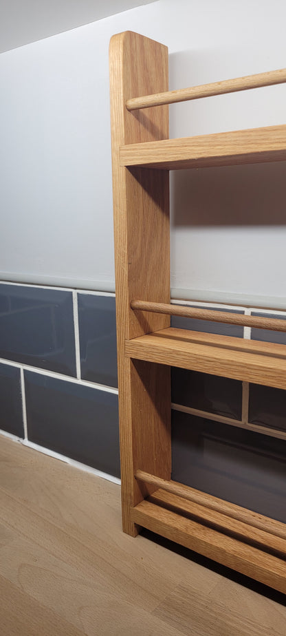 Side view of solid oak spice rack stood on a kitchen worktop under kitchen cabinets on a wall
