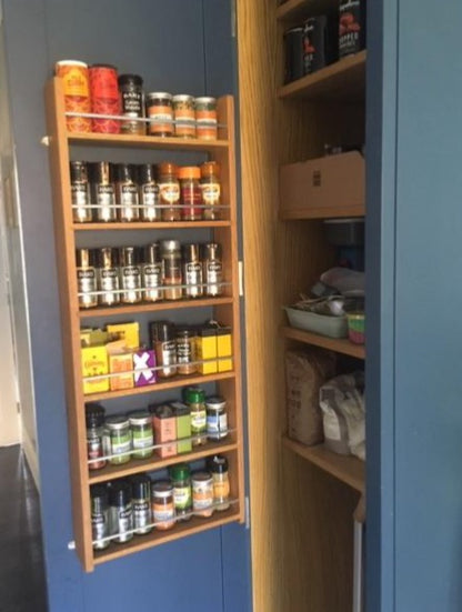 Solid oak spice rack fixed to a kitchen cabinet door filled with herb and spice jars